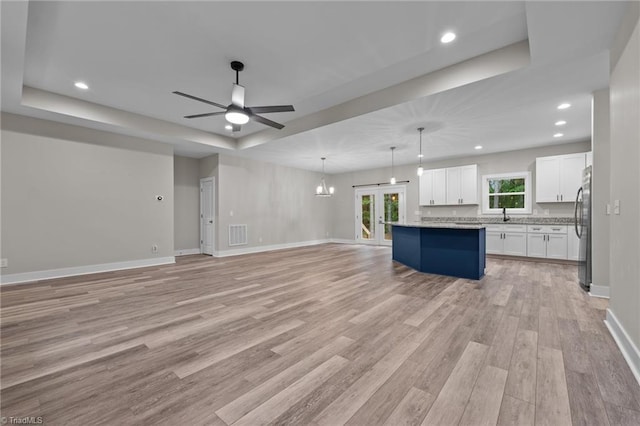 unfurnished living room featuring a raised ceiling, a ceiling fan, light wood-type flooring, recessed lighting, and baseboards