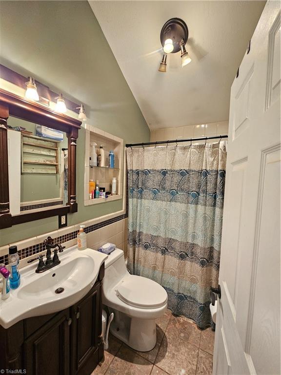 full bath with vanity, a shower with shower curtain, tile walls, toilet, and tasteful backsplash