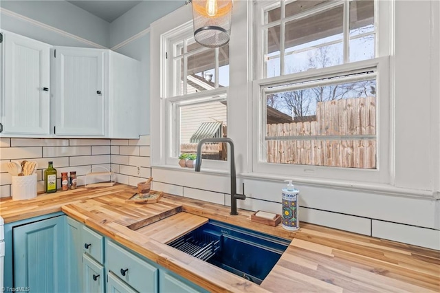 kitchen with white cabinets, sink, backsplash, blue cabinetry, and butcher block countertops