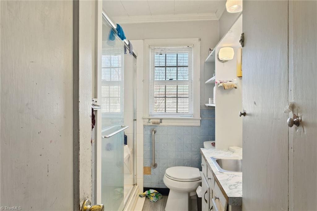 bathroom featuring vanity, a shower stall, crown molding, toilet, and tile walls