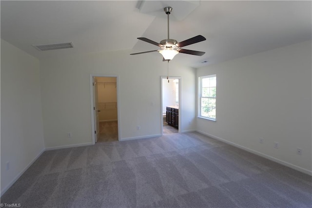 unfurnished bedroom featuring a walk in closet, ensuite bath, carpet floors, ceiling fan, and lofted ceiling