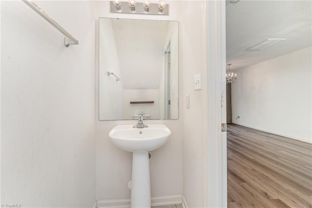 bathroom featuring a sink, a textured ceiling, wood finished floors, an inviting chandelier, and baseboards