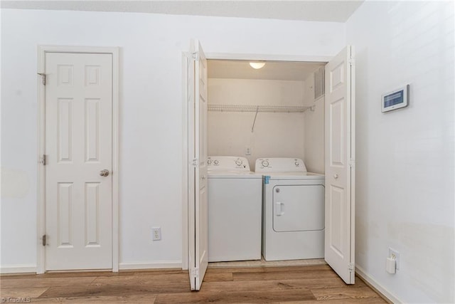 clothes washing area with laundry area, washing machine and dryer, baseboards, and light wood-style floors