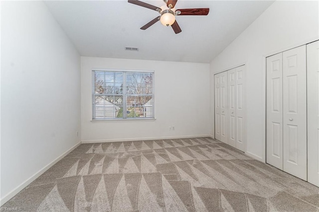 unfurnished bedroom featuring visible vents, two closets, baseboards, carpet, and lofted ceiling