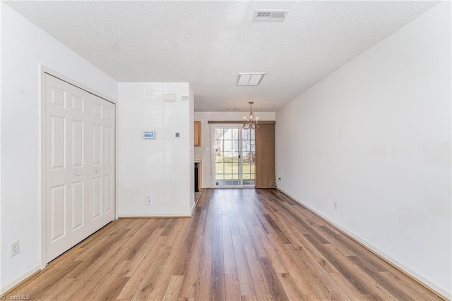 unfurnished room featuring visible vents, light wood-style floors, an inviting chandelier, and a textured ceiling