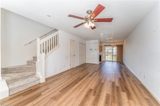 unfurnished living room with stairs, ceiling fan with notable chandelier, light wood finished floors, and a textured ceiling