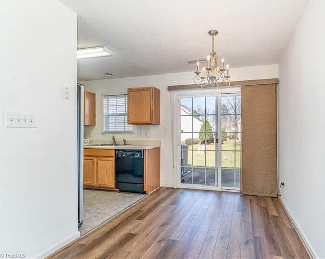 kitchen with a textured ceiling, black dishwasher, light wood finished floors, a chandelier, and light countertops