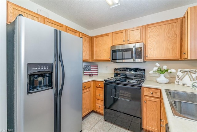 kitchen with light countertops, light tile patterned floors, appliances with stainless steel finishes, a textured ceiling, and a sink