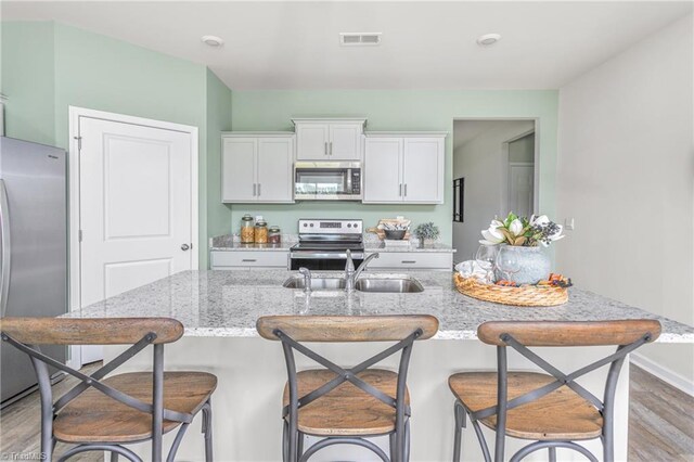 kitchen with a breakfast bar area, light stone countertops, light hardwood / wood-style floors, white cabinetry, and stainless steel appliances