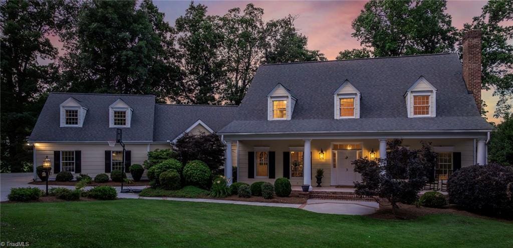 cape cod home featuring a porch and a yard