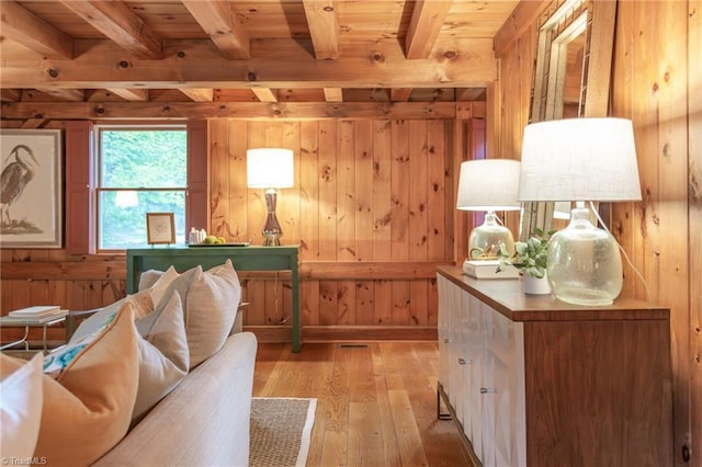 living area featuring beam ceiling, wood walls, and light wood finished floors