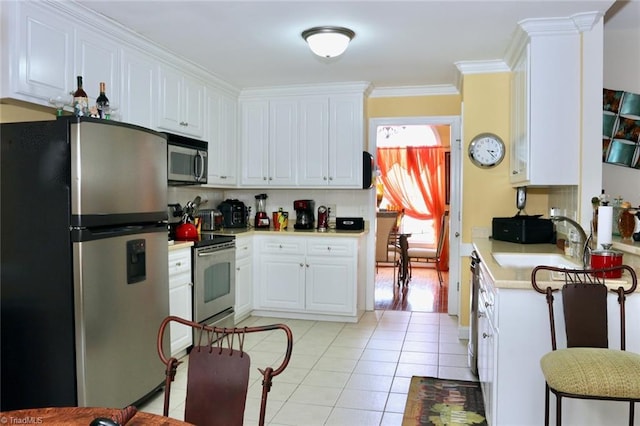 kitchen with appliances with stainless steel finishes, sink, white cabinetry, light tile patterned floors, and ornamental molding