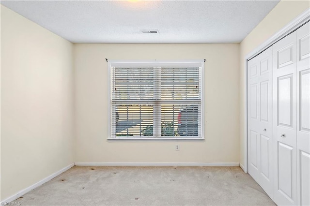 unfurnished bedroom with light carpet, a textured ceiling, and a closet