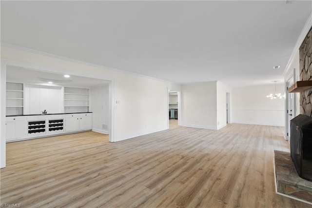 unfurnished living room with built in features, light wood-type flooring, crown molding, and an inviting chandelier