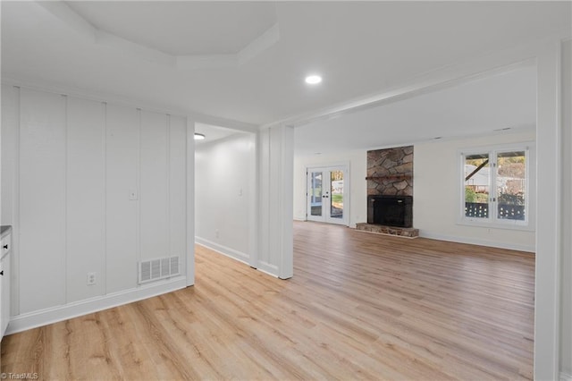 unfurnished living room with a tray ceiling, a stone fireplace, and light hardwood / wood-style flooring