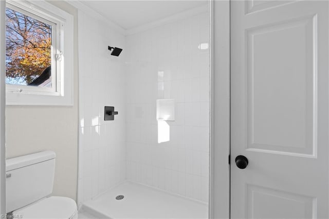 bathroom with a tile shower, toilet, and crown molding