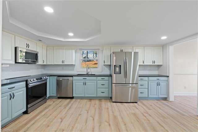 kitchen with sink, stainless steel appliances, a raised ceiling, white cabinets, and light wood-type flooring