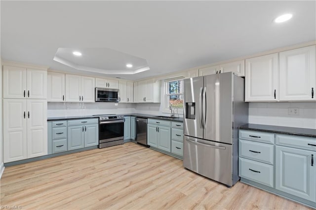 kitchen with a raised ceiling, sink, light wood-type flooring, white cabinetry, and stainless steel appliances