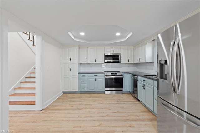 kitchen with light hardwood / wood-style floors, white cabinetry, appliances with stainless steel finishes, and a tray ceiling