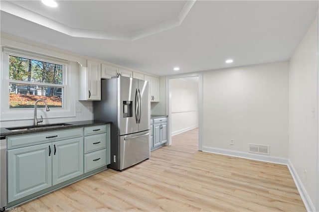 kitchen with a tray ceiling, sink, light hardwood / wood-style flooring, stainless steel fridge with ice dispenser, and white cabinetry