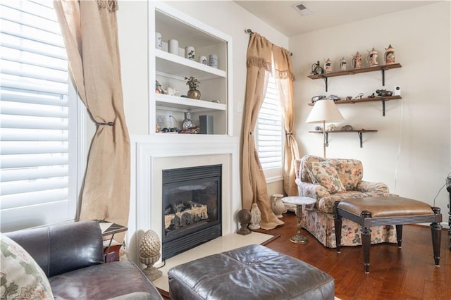 living area featuring wood-type flooring, built in shelves, and a healthy amount of sunlight