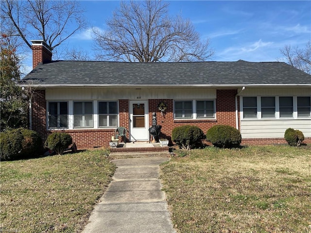 view of front facade featuring brick siding, a chimney, a front yard, and roof with shingles