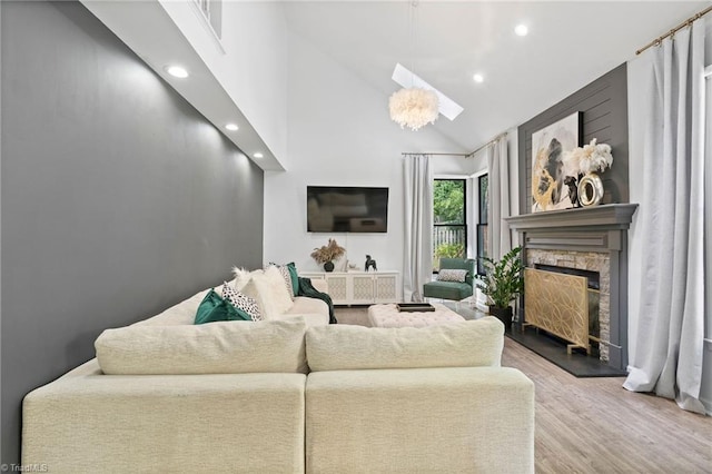 living room featuring high vaulted ceiling, a fireplace, wood finished floors, a skylight, and recessed lighting