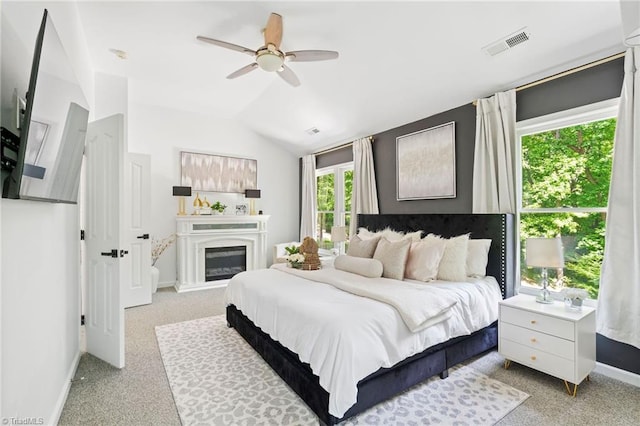 bedroom featuring light carpet, baseboards, a glass covered fireplace, lofted ceiling, and ceiling fan