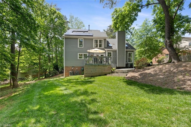 back of house featuring a lawn, roof mounted solar panels, a wooden deck, a chimney, and cooling unit