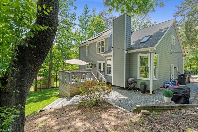 rear view of property with a deck, a chimney, and a shingled roof