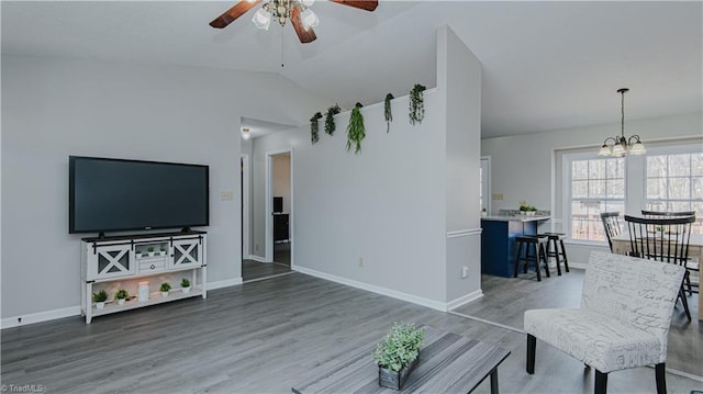 living room featuring vaulted ceiling, ceiling fan with notable chandelier, baseboards, and wood finished floors