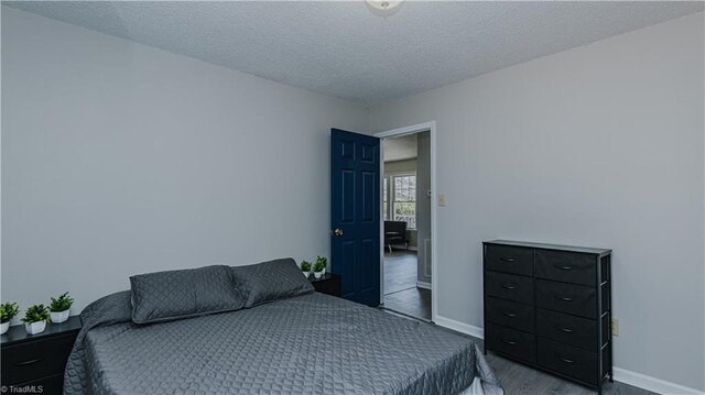 bedroom featuring a textured ceiling, baseboards, and wood finished floors