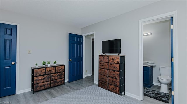 bedroom with ensuite bath, baseboards, and wood finished floors