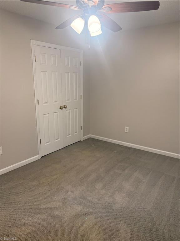 unfurnished bedroom featuring a closet, dark carpet, and ceiling fan