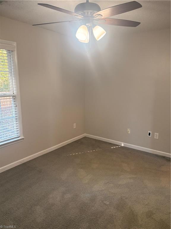 spare room with dark colored carpet and ceiling fan