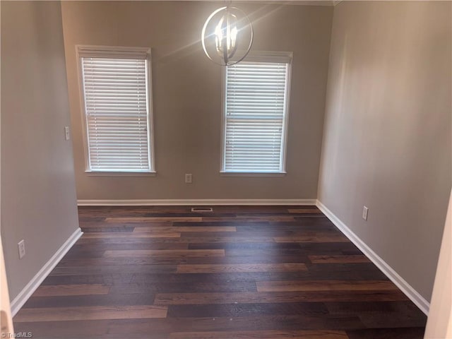 unfurnished room featuring dark wood-type flooring and a notable chandelier