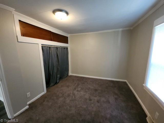 unfurnished bedroom featuring crown molding, a closet, and dark carpet