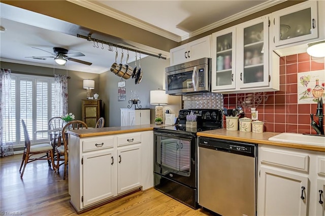 kitchen featuring a peninsula, a sink, ornamental molding, ceiling fan, and stainless steel appliances