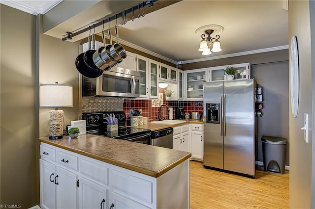 kitchen with a sink, tasteful backsplash, light wood-style floors, appliances with stainless steel finishes, and a peninsula