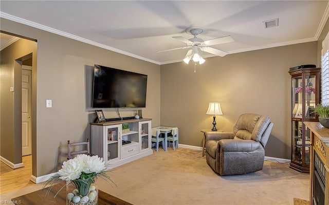 living area with a ceiling fan, visible vents, baseboards, ornamental molding, and carpet flooring