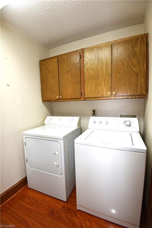 clothes washing area with cabinets, dark hardwood / wood-style flooring, a textured ceiling, and washing machine and dryer