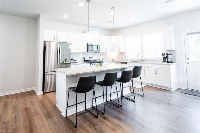 kitchen with a breakfast bar, a kitchen island, a sink, wood finished floors, and appliances with stainless steel finishes