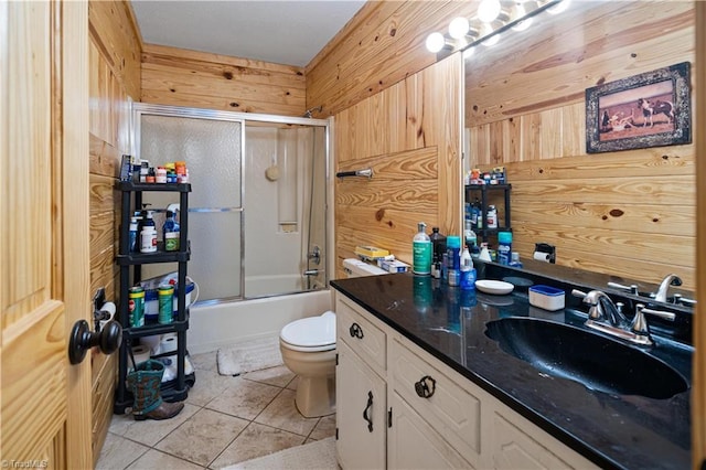 full bathroom with vanity, wood walls, shower / bath combination with glass door, tile patterned floors, and toilet