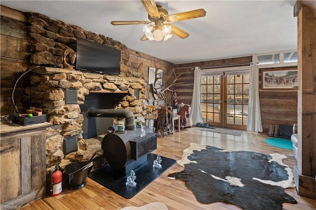 living room featuring french doors, ceiling fan, wooden walls, hardwood / wood-style flooring, and a wood stove