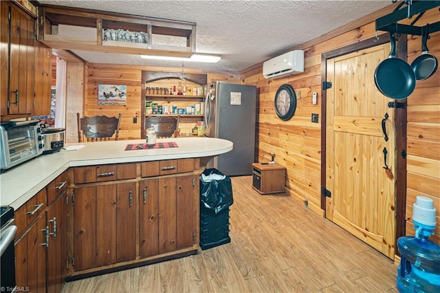 kitchen with kitchen peninsula, a textured ceiling, wooden walls, an AC wall unit, and stainless steel refrigerator