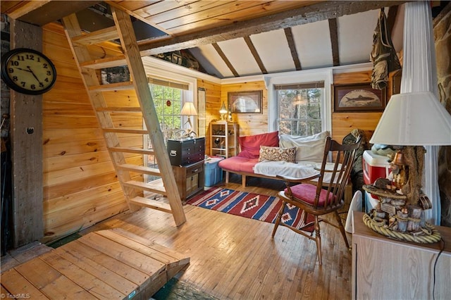 living area with vaulted ceiling with beams, wooden walls, plenty of natural light, and hardwood / wood-style floors