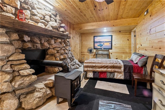 bedroom featuring ceiling fan, wood ceiling, wooden walls, and a wood stove