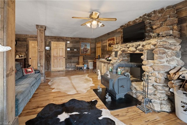 unfurnished living room featuring a wood stove, wooden walls, hardwood / wood-style flooring, ceiling fan, and decorative columns