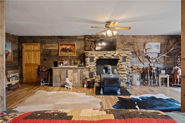 living room with a wood stove, wood walls, ceiling fan, and wood-type flooring