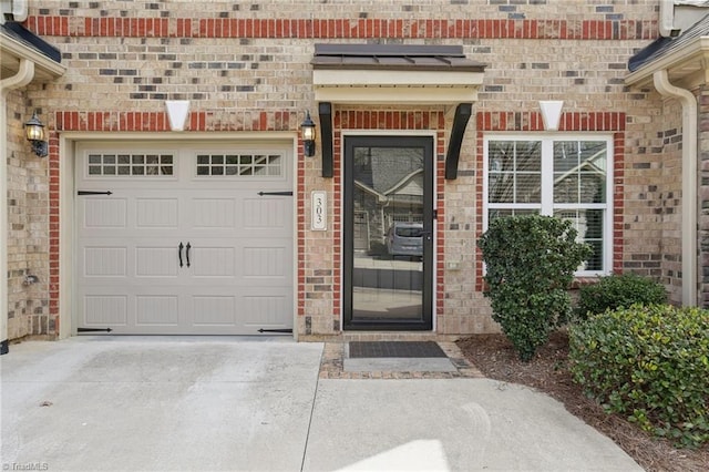 doorway to property with a garage, brick siding, and driveway